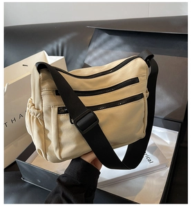 Detail of cream nylon crossbody bag featuring multi-zipper pockets and black adjustable strap