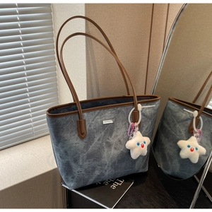 Détail du sac cabas en denim avec bordure en cuir marron et breloque étoile en peluche