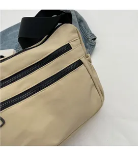 Close-up of beige nylon crossbody bag with dual parallel black zippers and woven strap