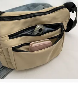 Detail view of khaki crossbody bag with multi-zipper compartments for organized storage