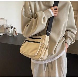 Detail of beige nylon crossbody bag with multiple zip pockets and wide black shoulder strap