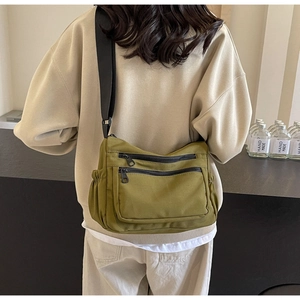 Detail of olive green nylon crossbody bag showing layered zip pockets and side drawstring pouch