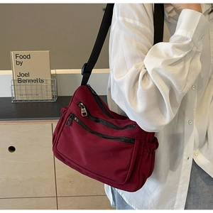 Detail of burgundy nylon crossbody bag featuring dual front zippers and side pockets