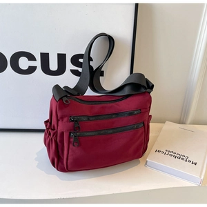 Fashionable burgundy nylon crossbody bag with multiple zippers and adjustable strap