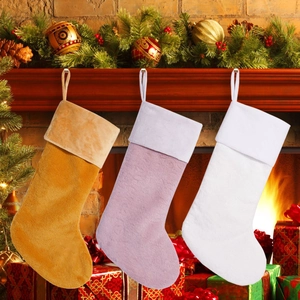 Drei Plüsch-Weihnachtssocken in Gold, Violett und Weiß hängen an einem gemütlichen Kamin