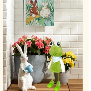 Detail of cute long-legged frog figurine with a blue plaid scarf in a garden setting