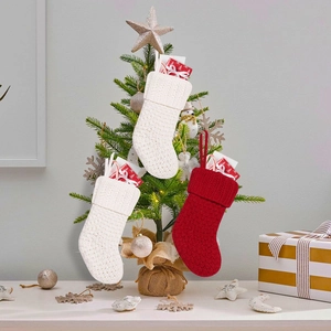 Knitted Christmas stockings with cable patterns hanging on a tree with festive gifts