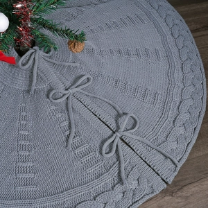Detailed knit texture and bow fasteners on gray Christmas tree skirt over wood floor