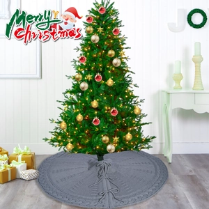 Grey knitted Christmas tree skirt with cable knit patterns and ribbon ties on floor