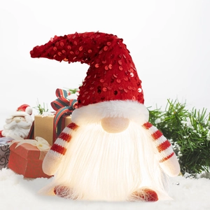 Detail of a glowing Christmas gnome with red sequin hat and warm LED light on snow