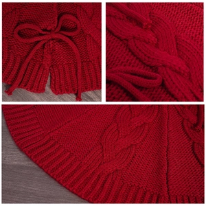 Red cable-knit Christmas tree skirt with decorative bow ties on grey wood background