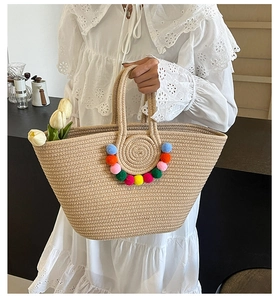 Detail of a large straw tote bag with colorful pom-poms and spiral woven pattern