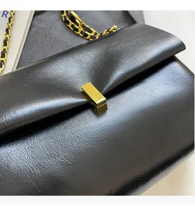 Dettaglio borsa in pelle lucida con chiusura rettangolare dorata e tracolla a catena