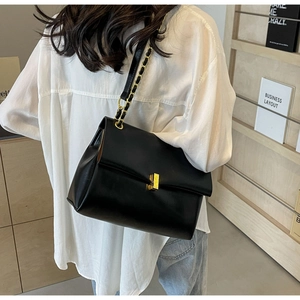 Dettaglio di una borsa a tracolla nera con catena dorata indossata dal modello