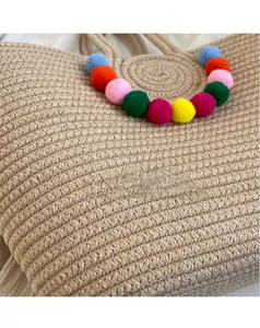Close-up of a woven straw tote bag with vibrant multi-colored pom-poms and boho texture