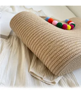 Close-up of beige woven straw tote bag with colorful pompom tassels on white background