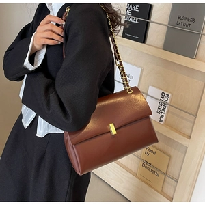 Dettaglio borsa in pelle marrone con chiusura dorata e tracolla a catena in metallo