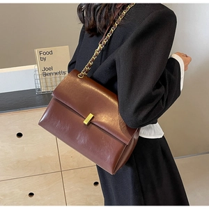 Dettaglio borsa a tracolla in pelle marrone vintage con fibbia dorata e catena su modella