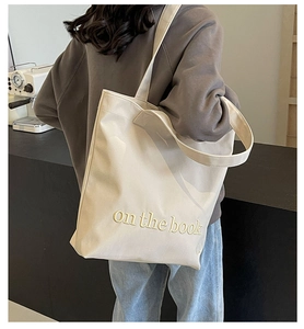 Close-up of beige canvas tote bag with 'on the book' yellow embroidery and wide strap