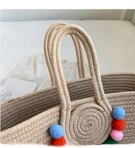 Close-up of beige woven straw tote bag with colorful decorative pom-poms and handles