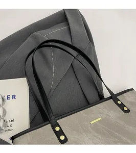 Detail of taupe fabric tote bag with black leather straps and gold metal hardware