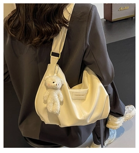 Beige pleated crescent tote bag detail with wide strap and plush bear pendant detail