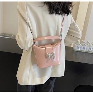 Détail du sac bandoulière en cuir verni rose avec nœud argenté sur un mannequin
