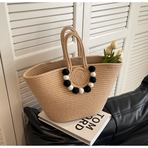 Detail of hand-woven straw tote bag with decorative black and white plush pompoms