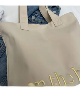 Detailed view of beige canvas tote bag with delicate yellow letter embroidery