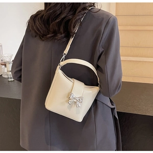 Détail d'un sac en cuir blanc crème avec boucle en nœud argenté et fine bandoulière réglable