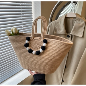 Detail of hand-woven straw tote bag with black and white pom pom charms and sturdy handle