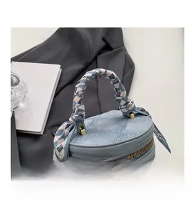 Détail du sac seau en denim bleu clair avec poignée en soie et plaque logo métallique