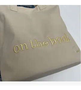 Detailed embroidery of 'on the book' text and book icon on beige canvas tote bag
