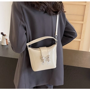 Détail d'un sac en cuir crème avec grande boucle de nœud argenté porté par un modèle