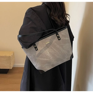 Detail of grey textured tote bag featuring black handles and elegant gold metal plaque