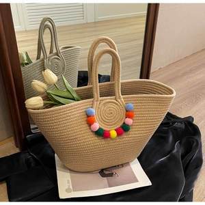 Detail of hand-woven straw tote bag featuring colorful pom-pom charms and double handles