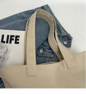 Close-up of beige tote bag wide handle featuring durable cross-stitch reinforced sewing