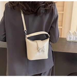 Détail d'un sac seau en cuir crème avec un nœud métallique argenté et une bandoulière réglable