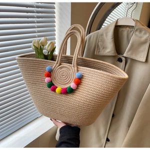 Close-up of woven straw tote bag featuring colorful pom-pom details and sturdy handles