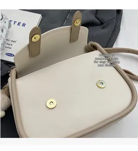 Detail view of cream saddle bag featuring dual magnetic closures and a plush pompom charm