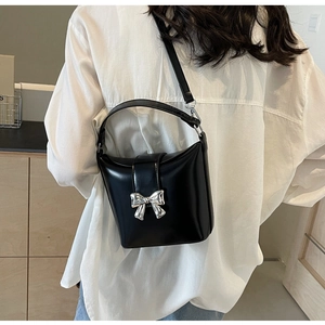 Détail d'un sac à main noir brillant avec boucle nœud argenté sur chemise blanche