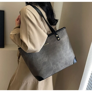 Close-up of distressed gray tote bag with black trim, leather patches and metal accents