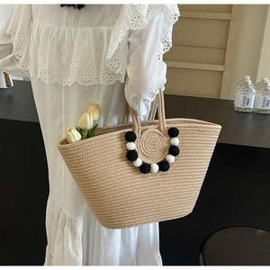 Detail of beige woven straw tote with decorative black and white pom-poms on the handle