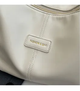 Detailed close-up of beige leather bag with gold embossed logo and premium stitching