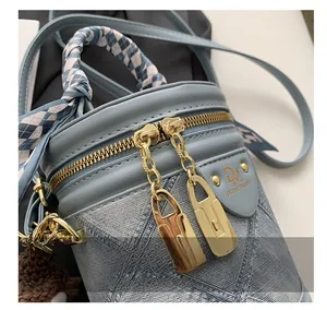 Détail du sac seau en denim bleu clair avec doubles zips dorés et poignée en foulard