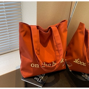 Detail of orange canvas tote bag with 'on the book' embroidery in a mirror reflection