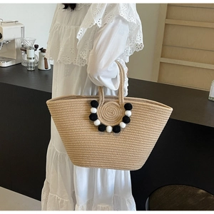 Detail of hand-woven straw tote with black and white pom-poms in a cafe setting