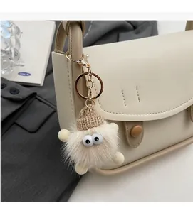 Close-up of a plush monster bag charm with big eyes and a brown knit hat on a beige bag