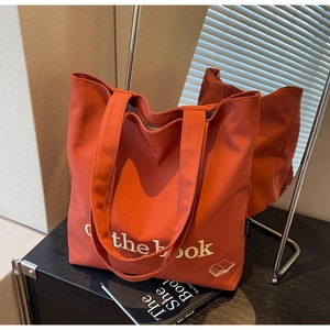 Detail view of large rust-orange canvas tote bag with 'the book' white embroidery