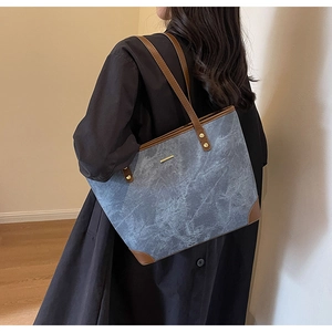 Detailed side view of large denim tote bag with brown leather handles on shoulder